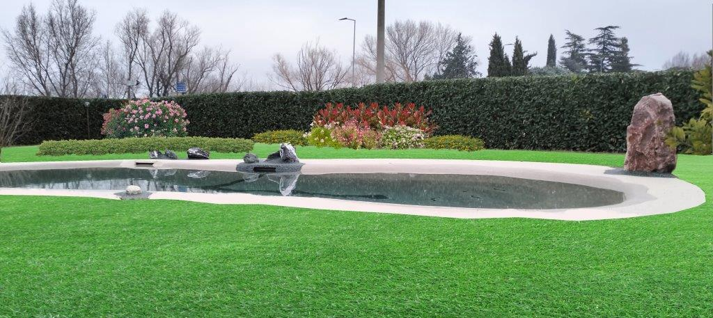 Piscina naturale nel giardino curato, con siepe e cespugli in fiore
