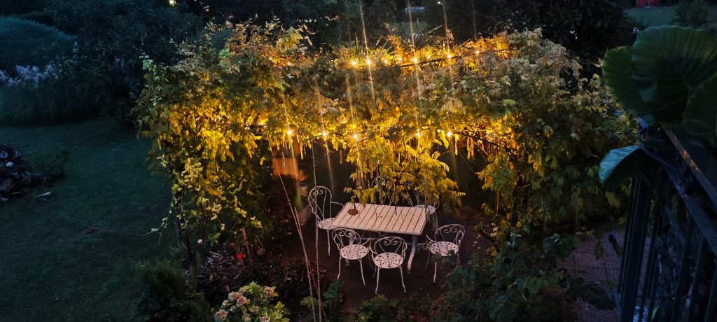 Tavolo e sedie bianche sotto la pergola del giardino, illuminata la sera