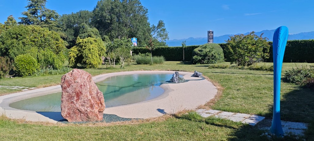 Piscina naturale con masso in pietra, prato e siepe sotto il cielo sereno
