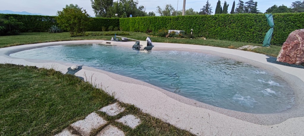 Piscina naturale nel prato, con siepe e masso in pietra