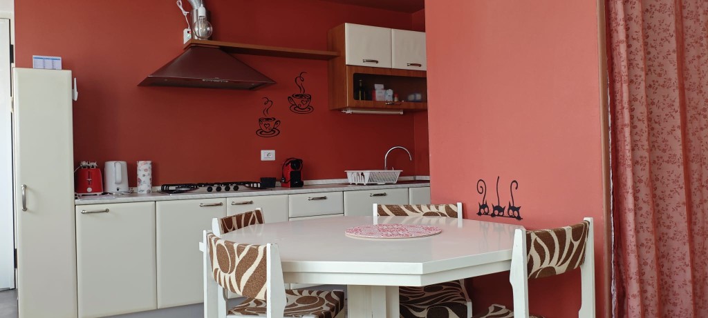 Cucina completa dell'appartamento 2.Rosso: piano cottura, elettrodomestici e zona pranzo con parete rossa