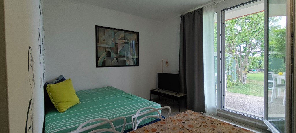 Appartamento 1.Verde — zona giorno con divano letto, Smart TV e porta finestra aperta sul giardino privato con tavolo