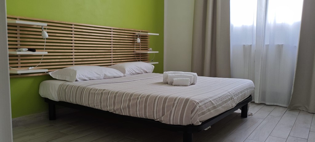 Apartament 1.Verde — sypialnia z łóżkiem małżeńskim, zieloną ścianą i oknem
